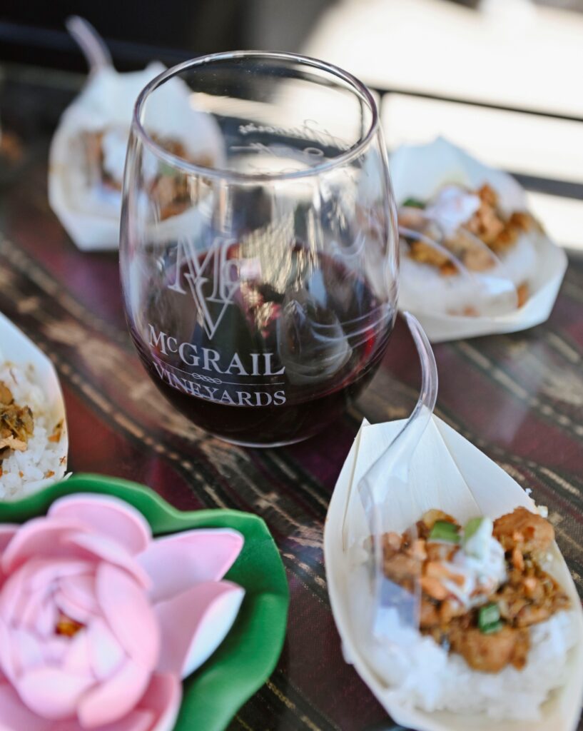 Glass of red wine at McGrail Vineyards served alongside small bites at an outdoor tasting table.