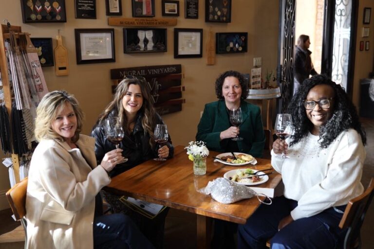 Group of four women enjoying a private wine tasting at McGrail Vineyards, seated together with glasses of wine and vineyard views in the background.