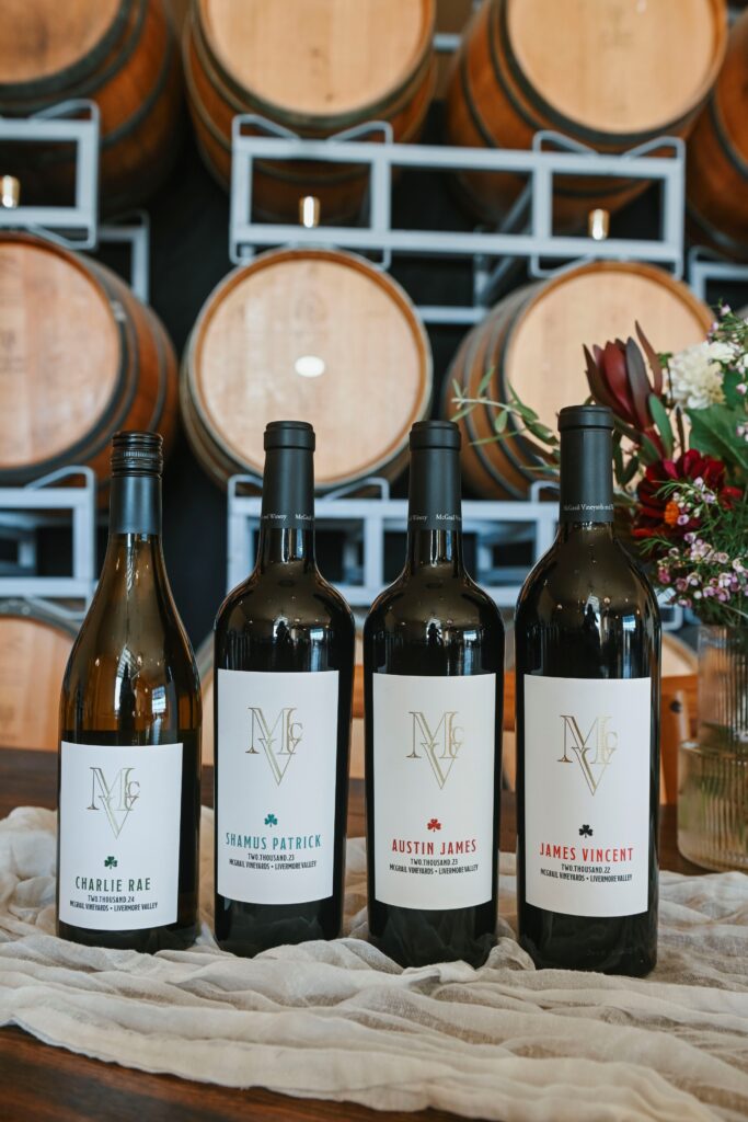 McGrail Vineyards wine bottles displayed outdoors with vineyard estate grounds and summer greenery in the background.