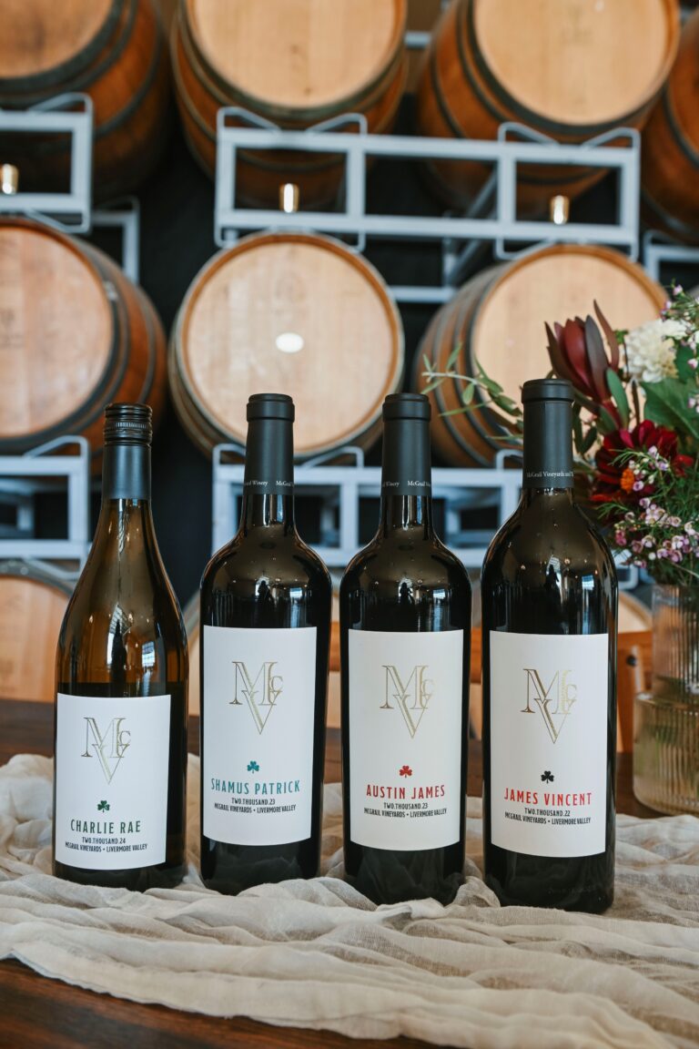 McGrail Vineyards wine bottles displayed outdoors with vineyard estate grounds and summer greenery in the background.