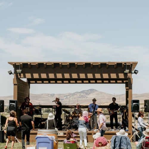Live band performing on an outdoor stage as guests enjoy music and wine at a vineyard lawn concert.
